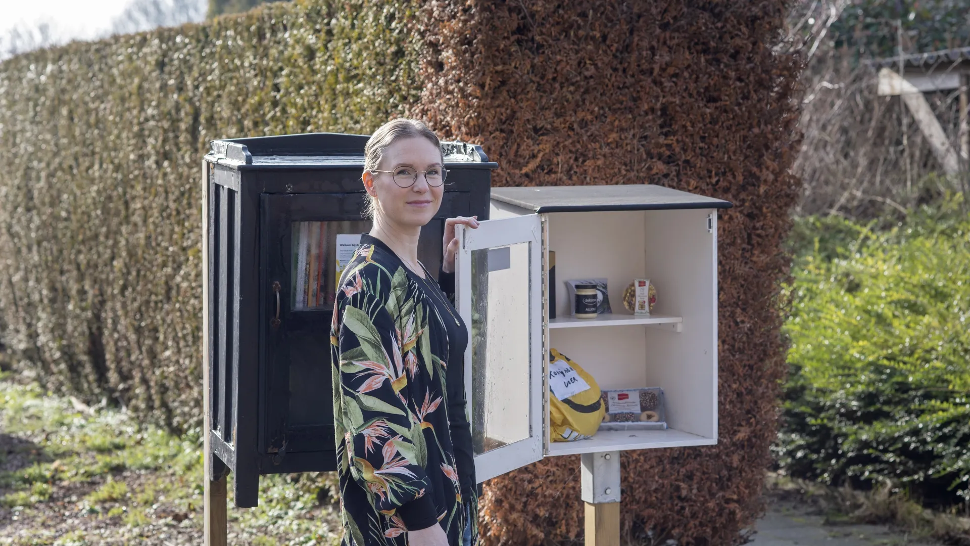 Een persoon bij een kleine open kast met boeken en spullen buiten.