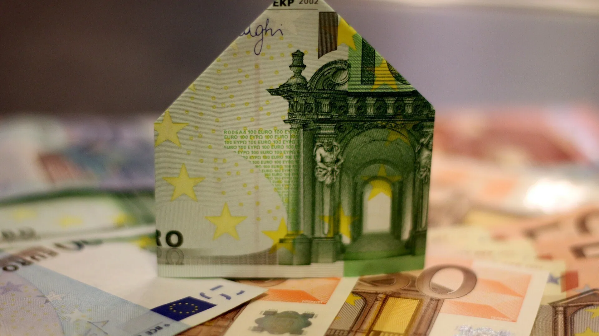 Een huisvormige vouw van een eurobiljet op een stapel eurobiljetten.
