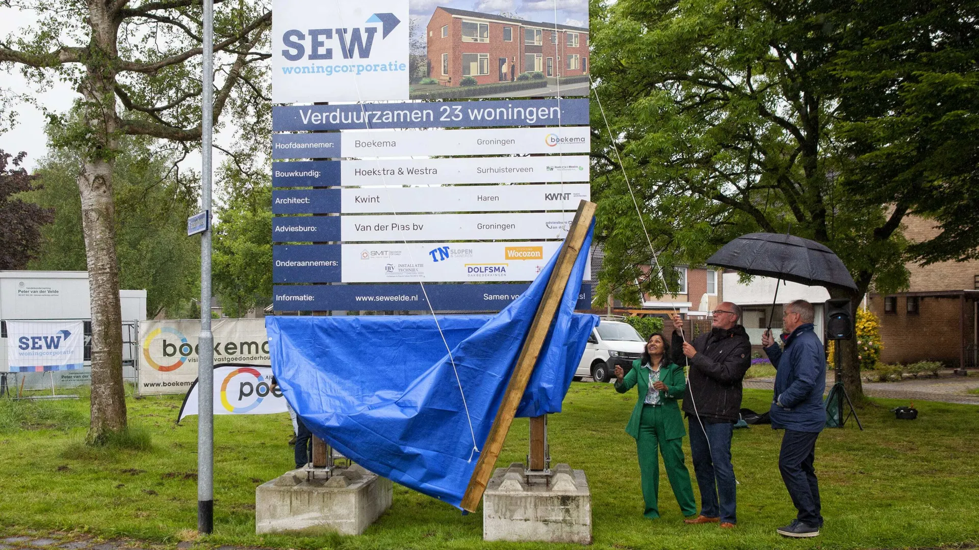 Mensen onthullen een bord voor een bouwproject onder een paraplu.