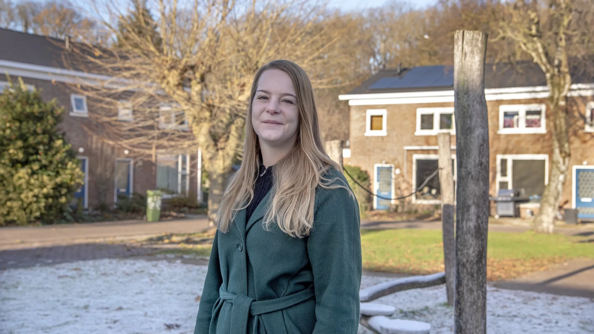 Een vrouw poseert in een buitenomgeving met huizen op de achtergrond.