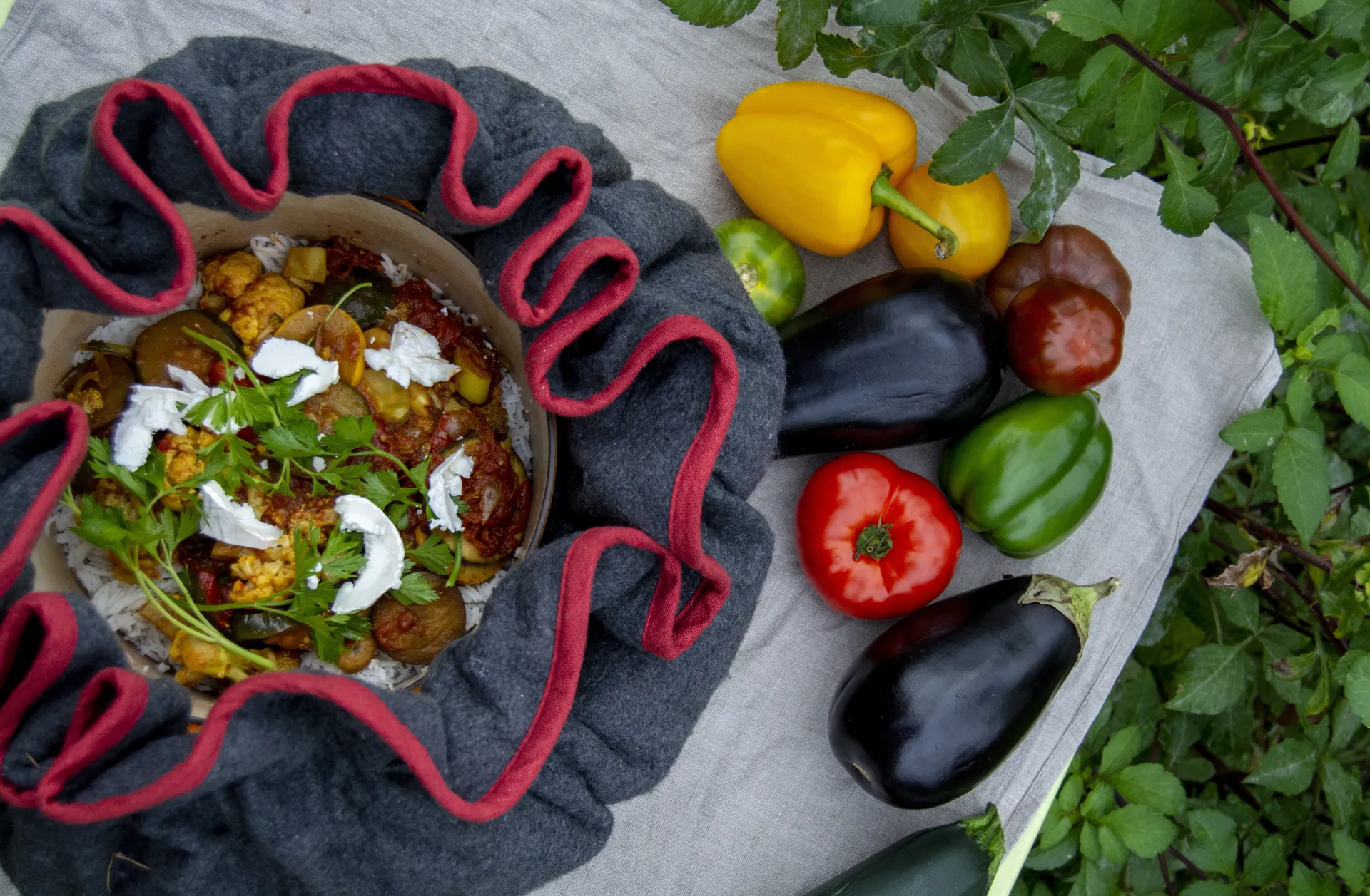 Een kleurrijk gerecht met groenten, omringd door verse paprika's en aubergines op een doek.