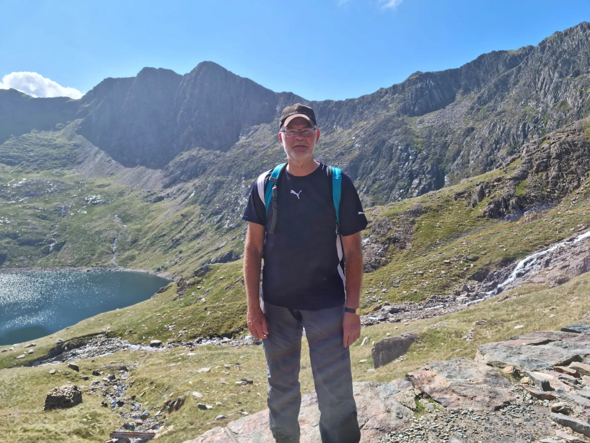 Man poseert voor berglandschap met helderblauwe lucht.