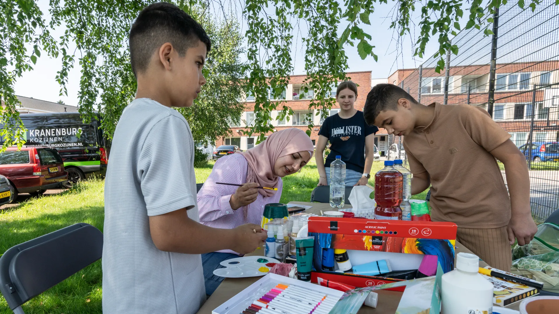 Kinderen nemen deel aan een knutselactiviteit buiten aan een tafel.