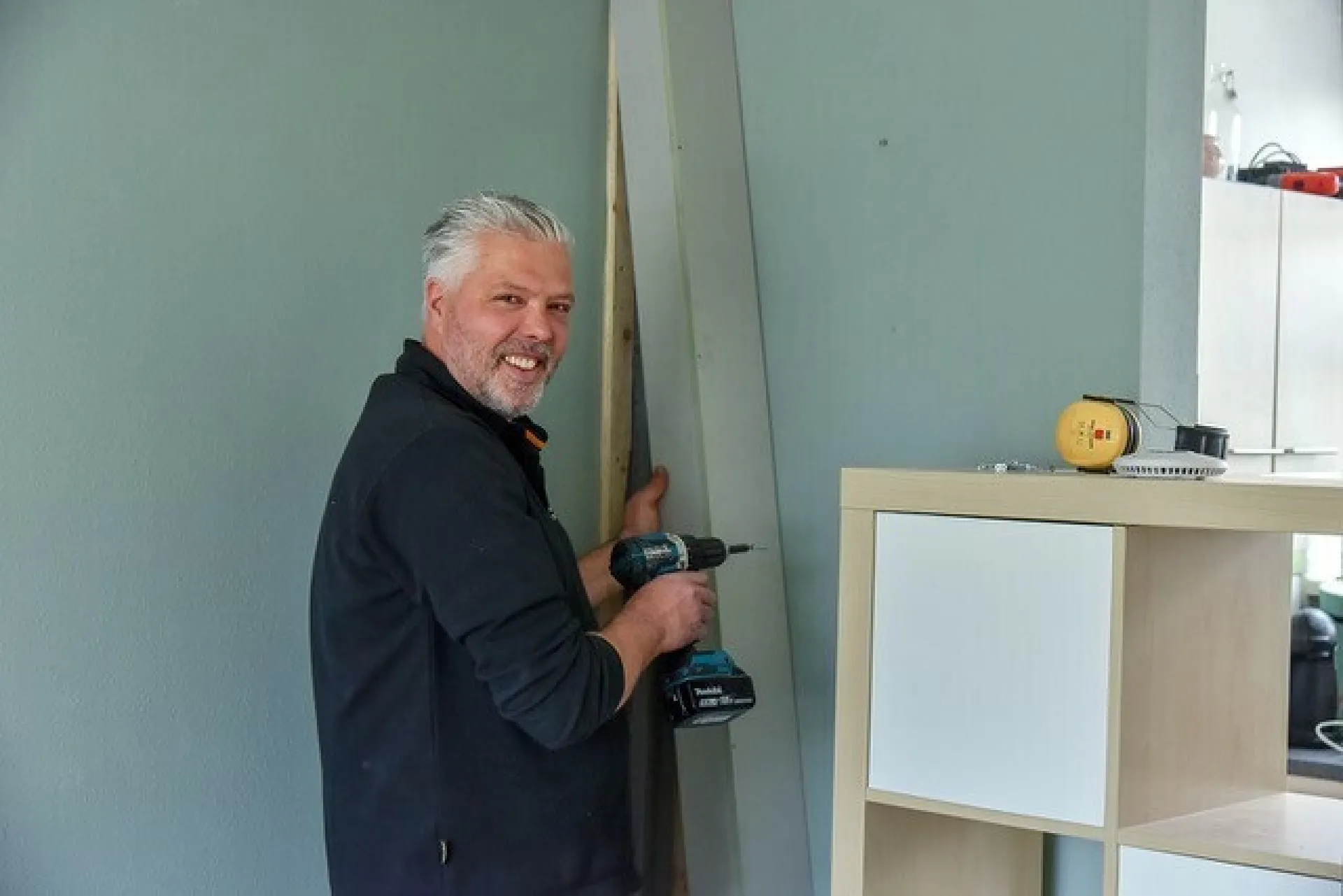 Man bezig met het boren van een plank aan een muur.