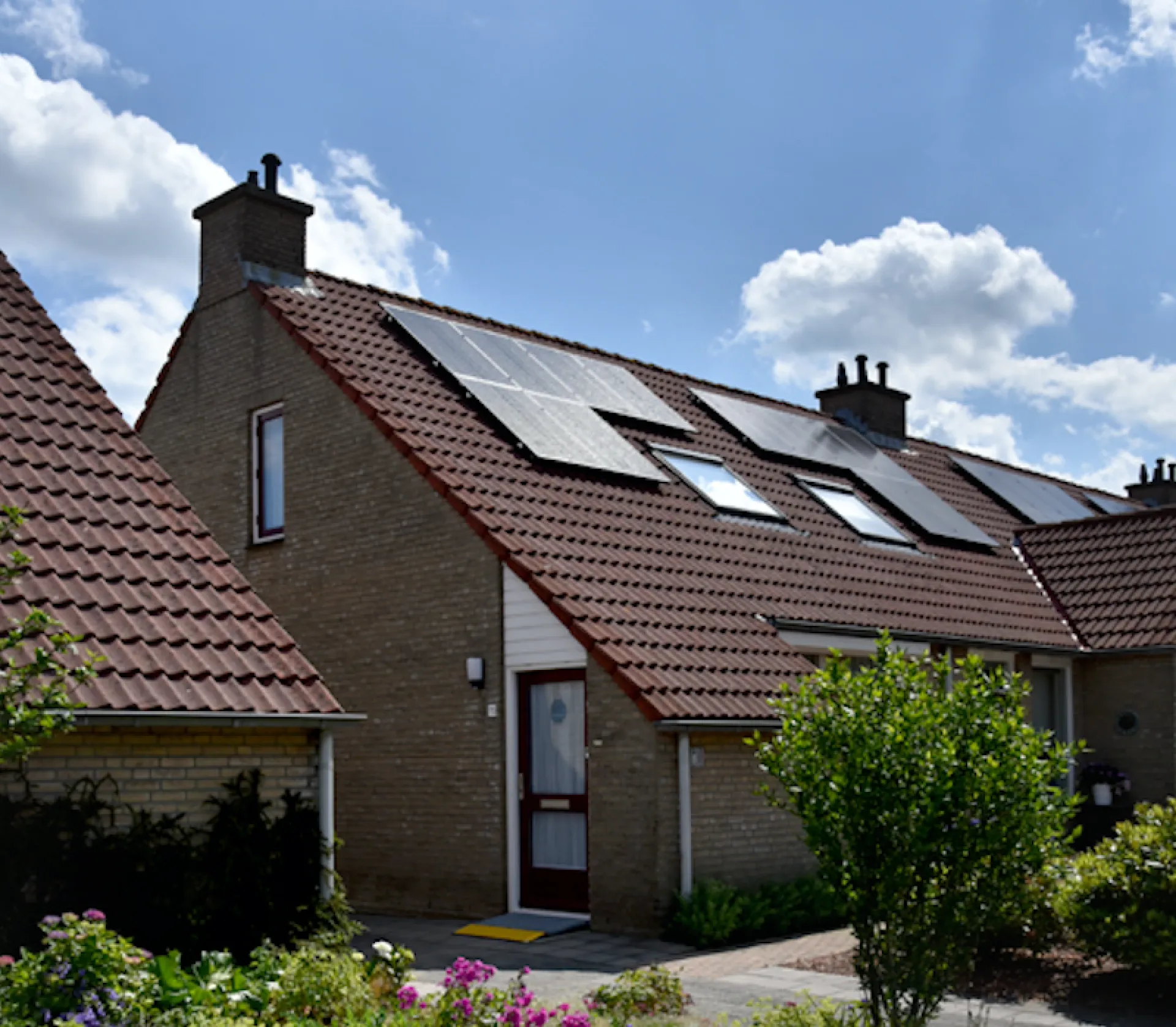 Rijtjeshuis met zonnepanelen en een tuin op een zonnige dag.